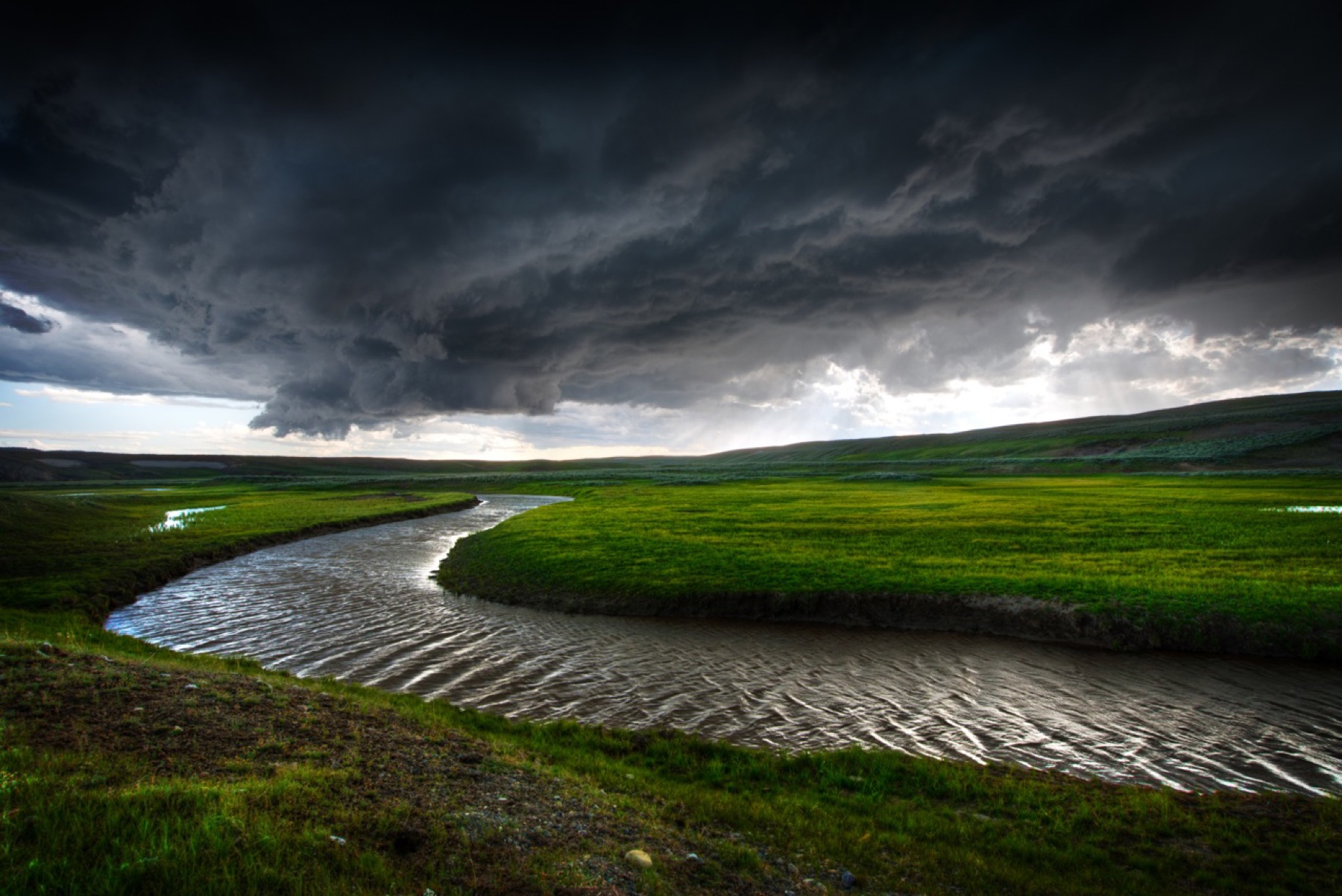 A winding river beneath a vast dark storm front in Hayden Valley