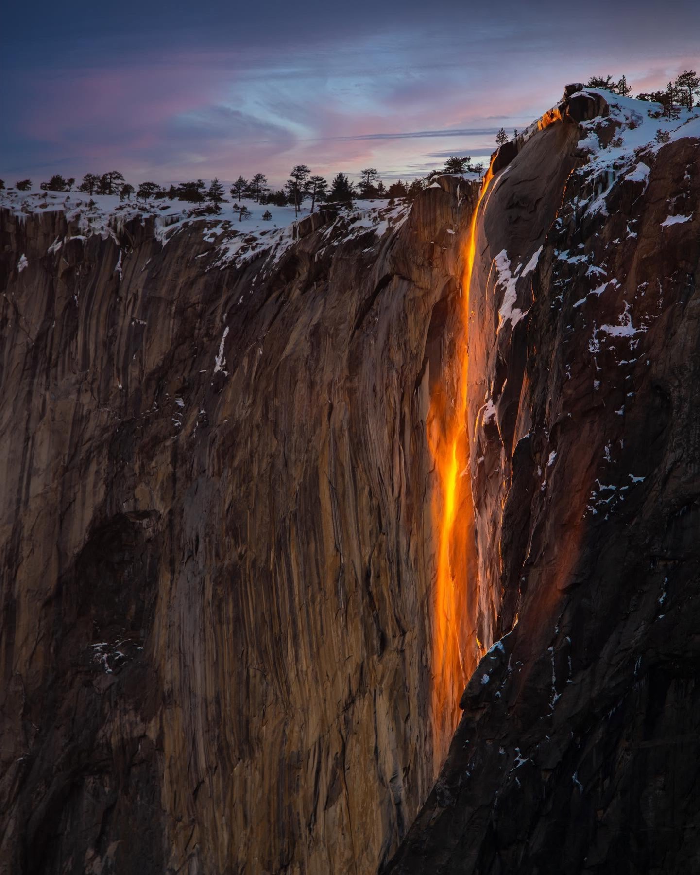 A narrow orange waterfall glowing against a dark granite cliff